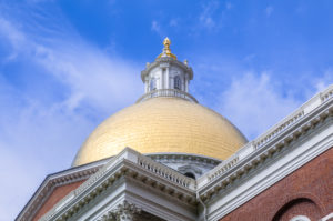 The Massachusetts State House, which is located on top of Beacon Hill in Boston, is a red brick neoclassical-federal style building. The 23 karat gold-gilded dome reflects the sun as does the gilt pine cone at the top of the white cupola. The pine cone was placed as a symbol of the abundant forests that made survival possible for the early settlers.